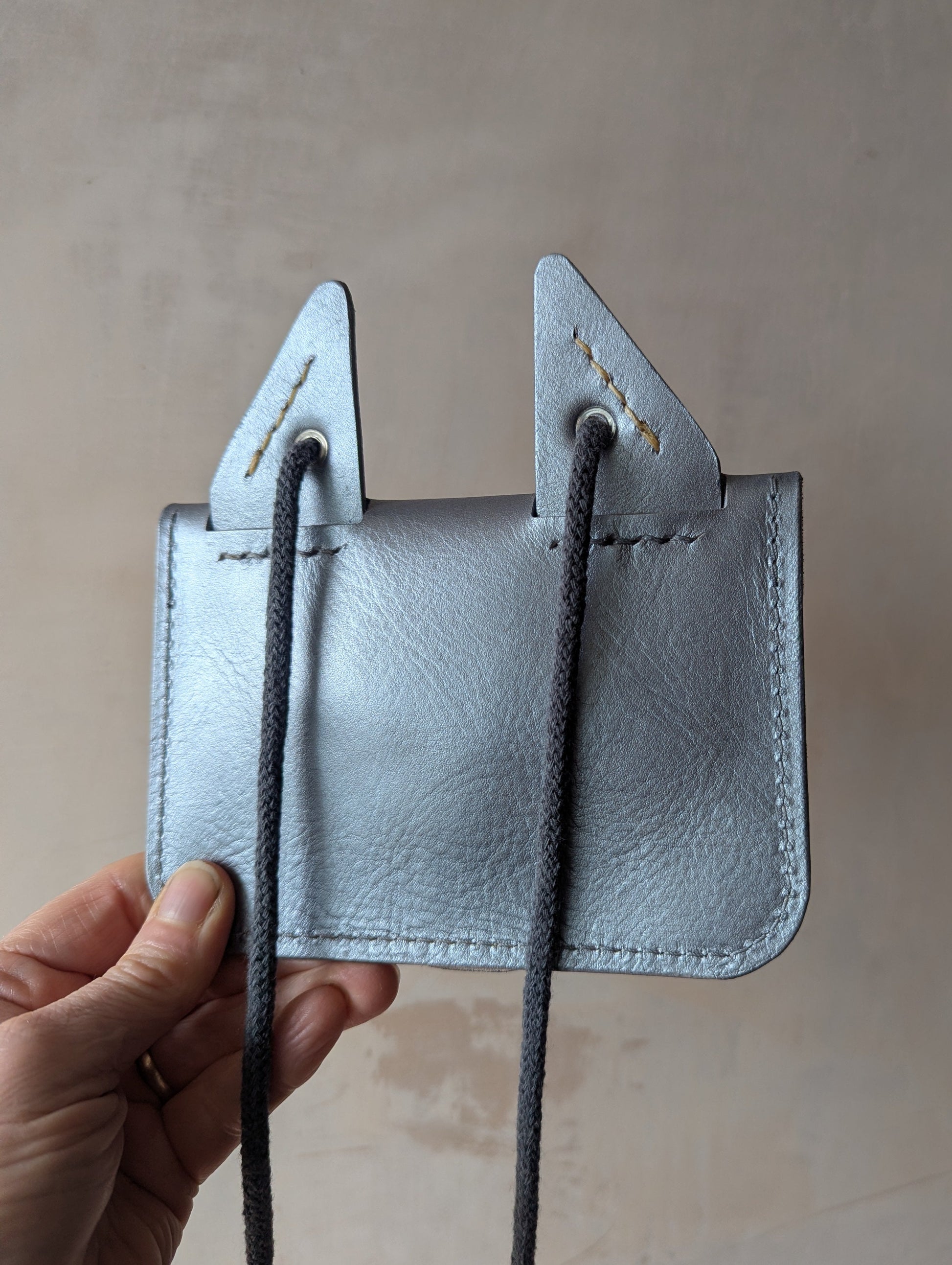 Silver leather fox purse with a strap held by a hand against a neutral background